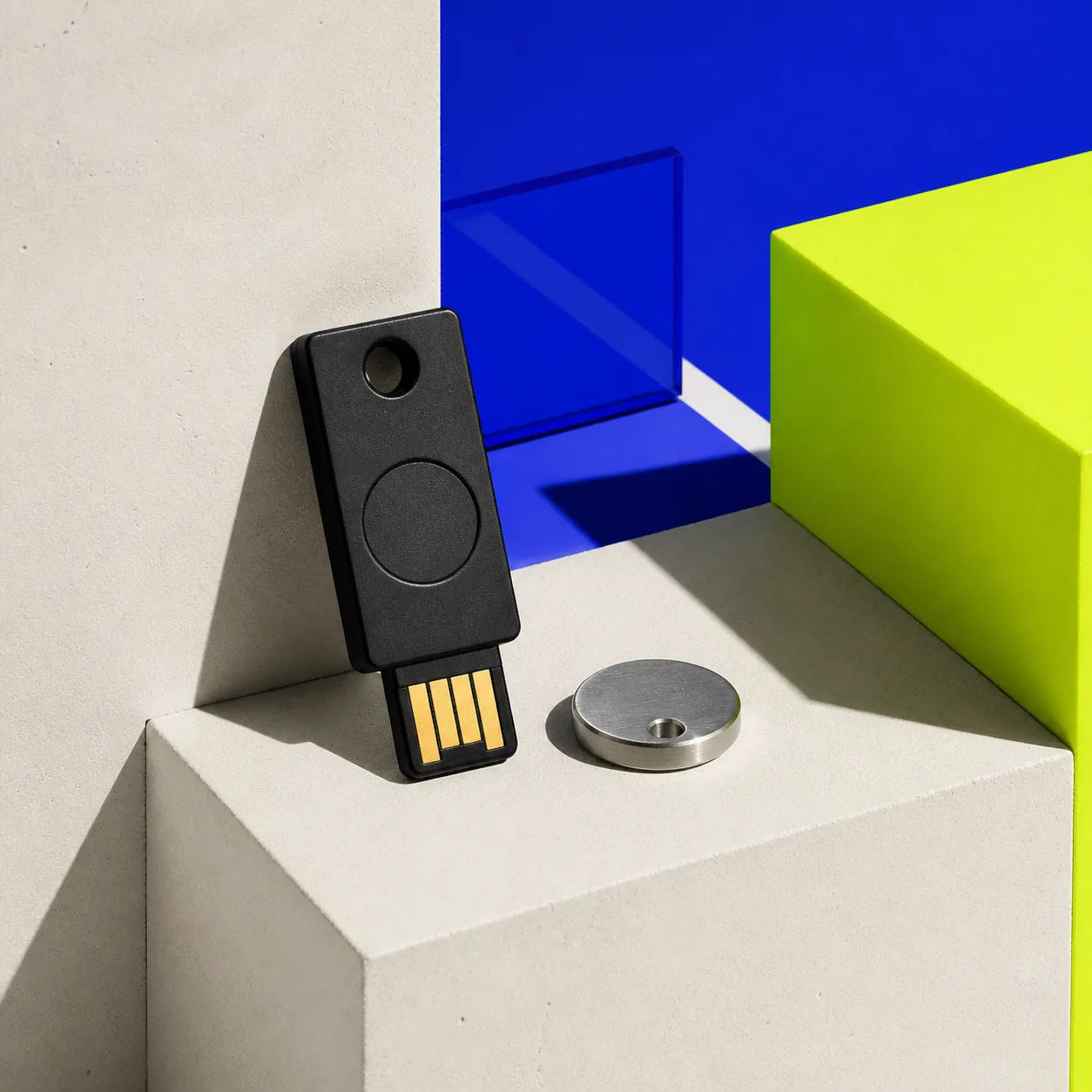 Black security key and metal token displayed on geometric blocks.